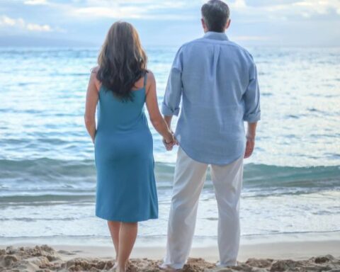 man and woman holding hands on beach, looking at the water