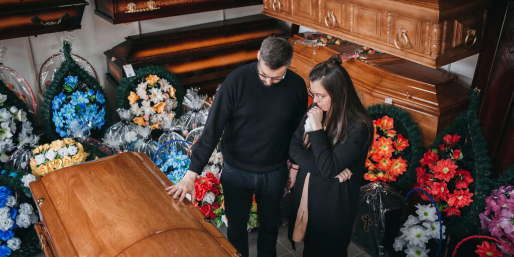 Man and woman grieving over casket surrounded by flowers