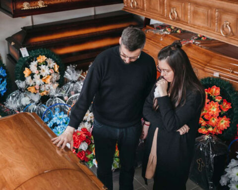 Man and woman grieving over casket surrounded by flowers