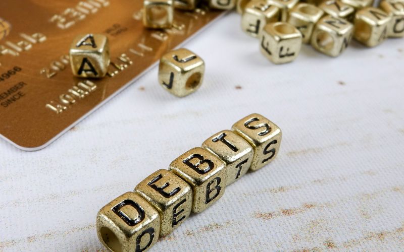 gold colored letter blocks spelling debts